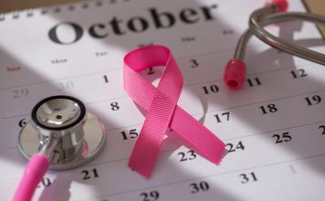A pink ribbon symbolizing breast cancer awareness placed on an October calendar alongside a stethoscope highlighting healthcare and awareness