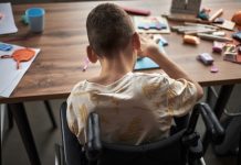 Child with disability engrossed in creating crafts while sitting at a cluttered table filled with art supplies and paper
