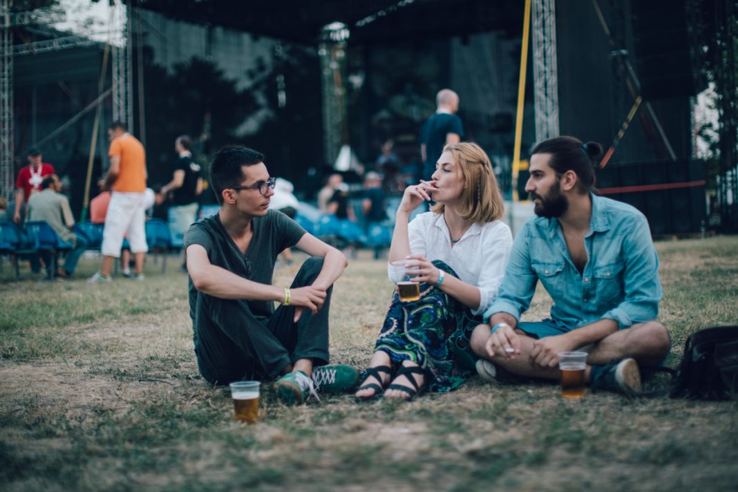 Festival vibes Group of friends sitting on the grass and drinking beer on music festival