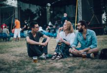 Group of friends sitting on the grass and drinking beer on music festival