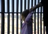 The effects of parental imprisonment on children’s education and health Adorable little girl holding her mother hand. Striped t-shirt worn by little girl. Iron bars in the background.