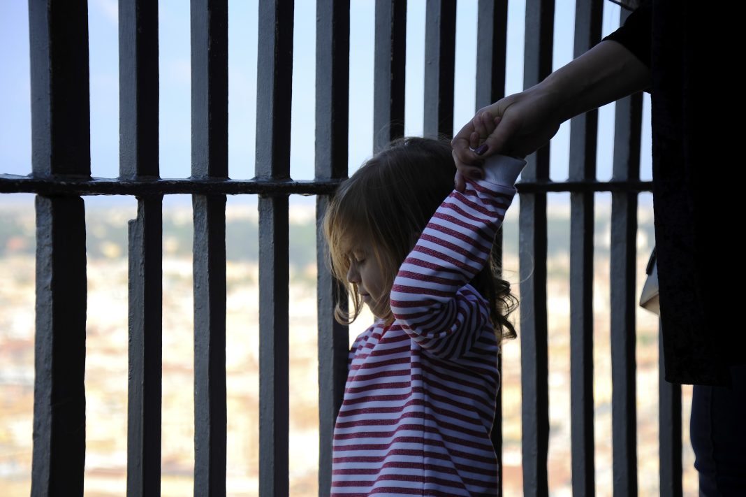 Adorable little girl holding her mother hand. Striped t-shirt worn by little girl. Iron bars in the background.