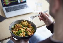 Close Of Man Eating Healthy Vegan Lunch At Office Deak Whilst Using Laptop