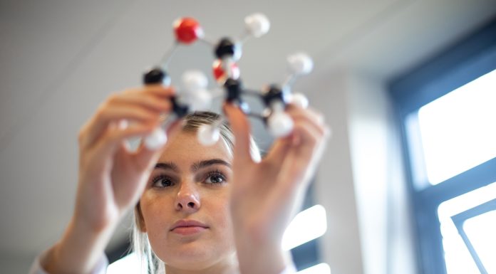 Close-up, shot through the hands of a female teenager examining a molecular chemistry set. She is wearing her school uniform.