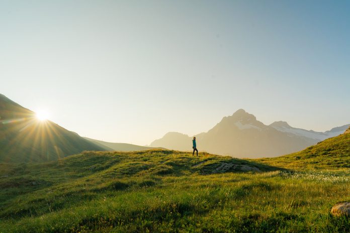 Woman hiking through the meadow in Swiss Alps in morning