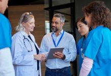 Medical mixed race team consulting with pharmaceutical representative at hospital hall. Healthcare hospital staff reviewing new pharmaceutical information. Doctors and nurses discussing healthcare advancements with businessman.