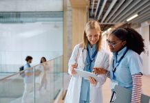 Happy female student doctors surfing the net on touchpad in a hallway at the university. Copy space.