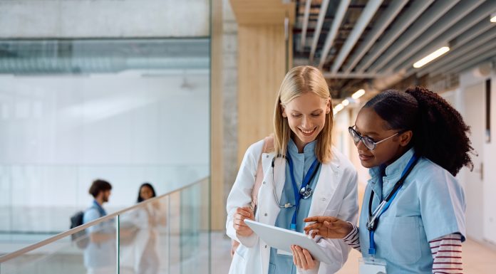 Happy female student doctors surfing the net on touchpad in a hallway at the university. Copy space.
