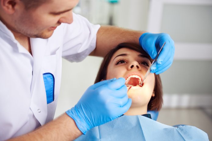 Male doctor in uniform checking up female patient's teeth in dental clinic. Concept of oral examination, toothache and decay treatment.