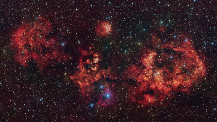 This image shows a cloud of gas and dust, shaped like a cosmic bat. The image was obtained mostly in visible light with the VLT Survey Telescope (VST), hosted at ESO’s Paranal Observatory in Chile. The intense red glow comes from hydrogen atoms ionised by the intense radiation of young stars within the cloud. The image also includes additional infrared data captured by ESO’s Visible and Infrared Survey Telescope for Astronomy (VISTA), also at Paranal. The most prominent clouds here are RCW 94, which represents the right wing of the bat, and RCW 95, which forms the body, while the other parts of the bat have no official designation. Credit: ESO/VPHAS+ team/VVV team This image shows a cloud of gas and dust, shaped like a cosmic bat. The image was obtained mostly in visible light with the VLT Survey Telescope (VST), hosted at ESO’s Paranal Observatory in Chile. The intense red glow comes from hydrogen atoms ionised by the intense radiation of young stars within the cloud. The image also includes additional infrared data captured by ESO’s Visible and Infrared Survey Telescope for Astronomy (VISTA), also at Paranal. The most prominent clouds here are RCW 94, which represents the right wing of the bat, and RCW 95, which forms the body, while the other parts of the bat have no official designation. Credit: ESO/VPHAS+ team/VVV team