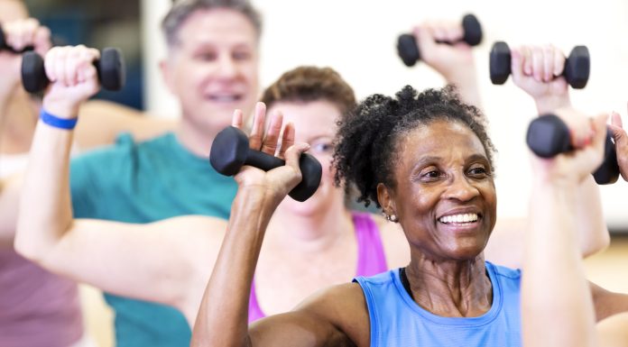 Close-up of a senior African-American woman in her 60s enjoying an exercise class. She is with a multiracial group of mature adults sitting on fitness balls and lifting hand weights.