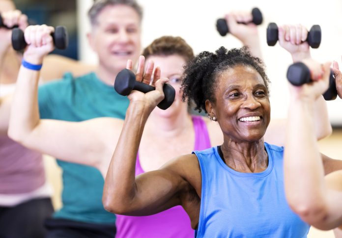 Senior African-American woman in exercise class Close-up of a senior African-American woman in her 60s enjoying an exercise class. She is with a multiracial group of mature adults sitting on fitness balls and lifting hand weights.