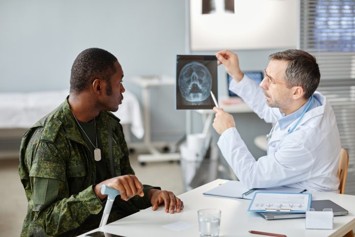 Professional medical worker showing skull x-ray picture to young adult military officer during appointment in hospital