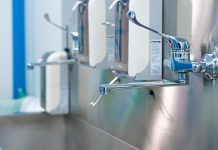 Selective focus on a shiny faucet of a sterile steel washbasin in a modern operating room. Hand washing room in a hospital.