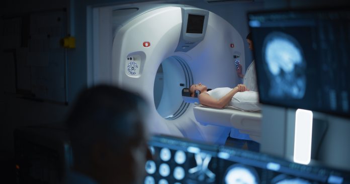 In Medical Laboratory Patient Undergoes MRI or CT Scan Process, in Control Room Doctor Watches Procedure and Monitors with Brain Scans Results. Healthcare Facility with High-Tech Equipment