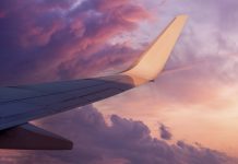 View of the wing of a flying airplane in the purple clouds of the setting sun and empty space for text