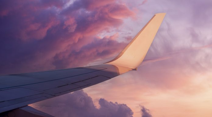 View of the wing of a flying airplane in the purple clouds of the setting sun and empty space for text