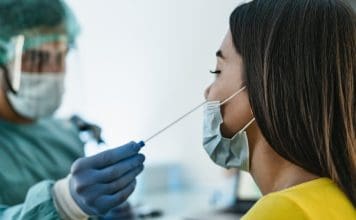 Medical worker wearing personal protective equipment doing corona virus swab on female patient - Covid19 test and health care concept