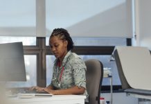 Side view shot of a female general practitioner sitting at her desk with a computer, typing on her keyboard.