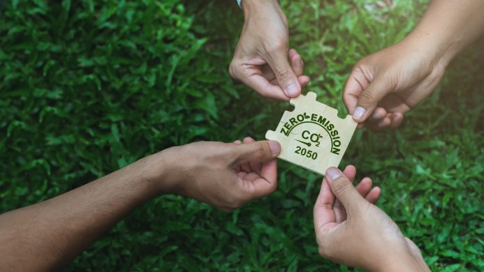 Four businessmen's hands holding a jigsaw puzzle with the words Net Zero on a green background. Concept, goal, zero greenhouse gas emissions. and long-term climate-neutral strategies.