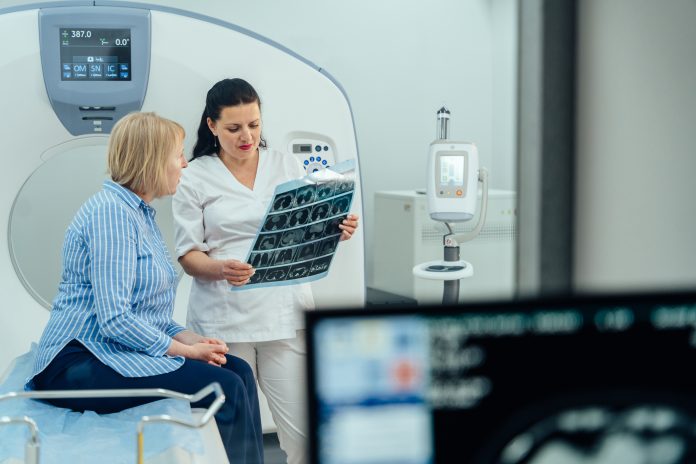 A woman is sitting in a hospital room with a doctor looking at a medical image