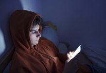 eenager using a smartphone lying in bed late at night