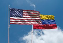 US and Venezuela flags above blue sky. USA and Venezuela confrontation