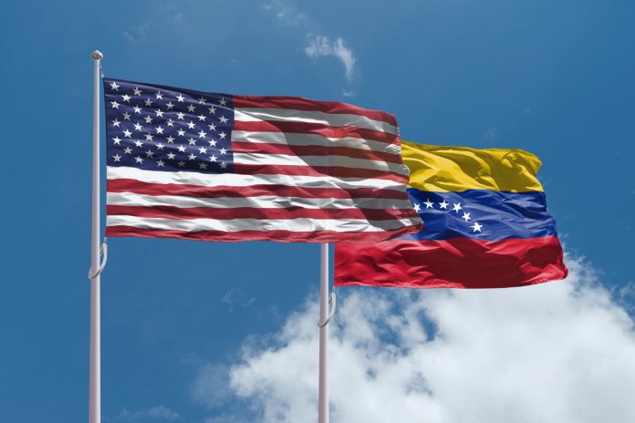 US and Venezuela flags above blue sky. USA and Venezuela confrontation