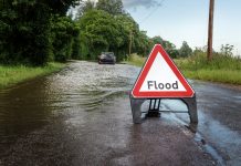county road in essex of flooded road closed due to severe rain with car stuck in the middle of road