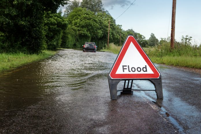 county road in essex of flooded road closed due to severe rain with car stuck in the middle of road