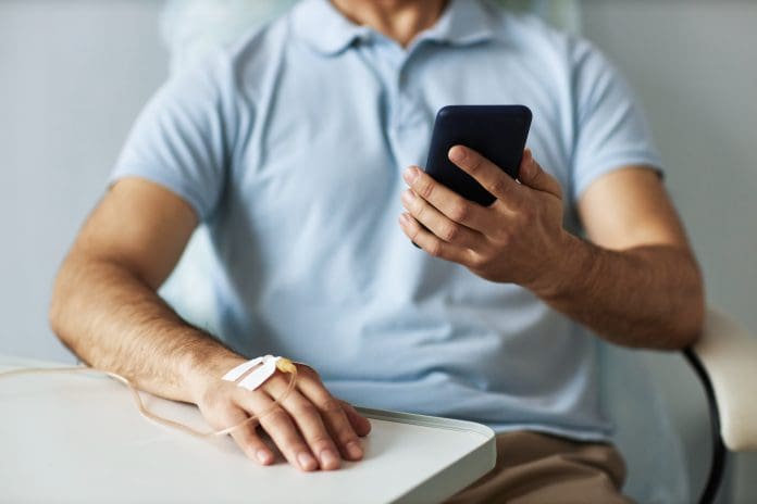 Closeup of unrecognizable man using smartphone during chemotherapy treatment, copy space