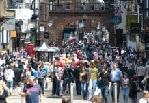 New government funding to revive Britain’s high streets A vibrant scene of Chester High Street, bustling with shoppers and tourists. The street is lined with historic Tudor-style buildings, featuring distinctive black-and-white timber framing. People can be seen exploring the variety of shops, cafes, and local businesses that add to the lively atmosphere. The combination of charming architecture and a busy pedestrian area creates a dynamic and welcoming environment.