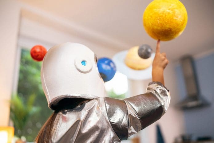 Girl in a space suit playing at home, exploring and learning about planets, imagining space travel.
