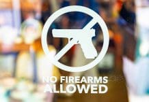 A close-up view captures a No Firearms warning sign prominently displayed on a transparent glass entrance door.