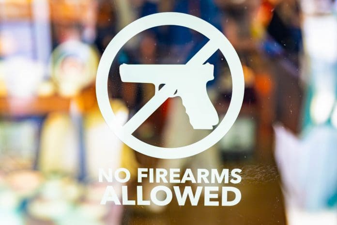 A close-up view captures a No Firearms warning sign prominently displayed on a transparent glass entrance door.